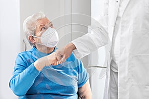 Female Senior adult with ffp2 mask is giving a doctor a fist bump