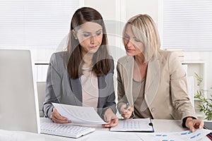 Female senior and junior managers sitting at desk working together in a business team.