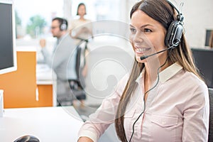 Female service desk consultant talking on hands-free phone in call center.