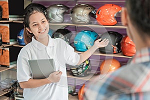 Female shop assistant holding the tablet in a hand gesture offered the helmet to male consumers