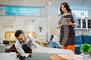 female shop clerk uses a tablet while male clerk adjusts the chairs