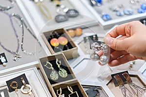female shopper carefully picks out a handcrafted earring from a vibrant collection of handmade jewelry on a market stall