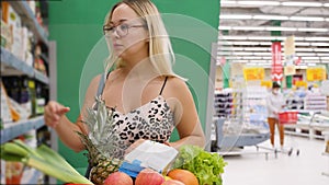 Female shopper with a trolley in the aisle of a store with a shopping list while shopping for food. Woman reading in her