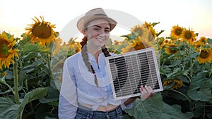 Female shows symbol of approval in backlight keeps in hand solar battery, joyful girl hold solar panel near field of