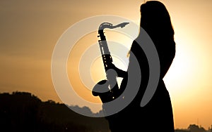 Female silhouette against the dawn with a saxophone in his hands