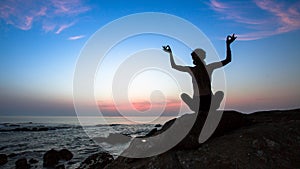 Female silhouette practicing yoga on the ocean cliff beach