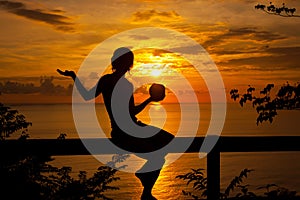 female silhouette in romantic sunset time on Caribbean coast with coconut drink in her hand