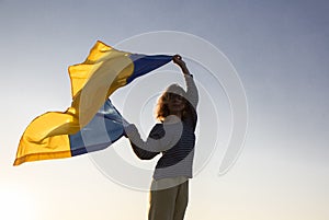 Female silhouette with the Ukrainian flag fluttering in the wind against the sky