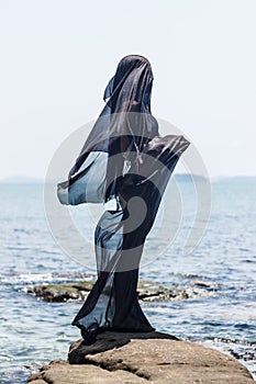 Female silhouette wrapped in black fabric posing at the rocky seaside