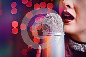 Woman singer with disco mic on bokeh light background.