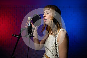 female singer sings into microphone with pop filter in recording studio