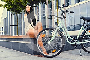 Female sits on a bench over modern building background after bicycle ride.