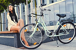 Female sits on a bench over modern building background after bicycle ride.