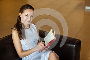 Female sitting on black sofa in white luxury dress and taking notes