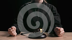 Female sitting at the desk with wooden hammer, dark room bright spotlight. Woman judge silhouette in the court room