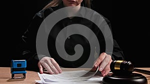 Female sitting at the desk with wooden hammer, dark room bright spotlight. Woman judge silhouette in the court room