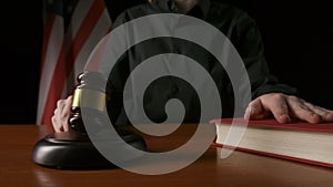 Female sitting at the desk with wooden hammer and law book, USA flag at the background. Woman judge in the court room