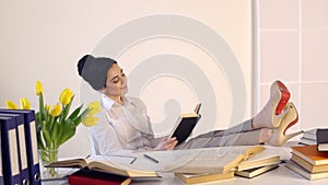 Female sitting at her workplace and laughing while reading holding book