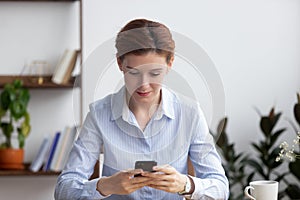 Female sitting in office room holding smartphone reading message