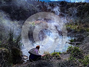 Female sitting on a river bank in the mist, Rotorua, New Zeland