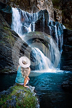 Female sitting by a tumbling waterfall and natural rock pool