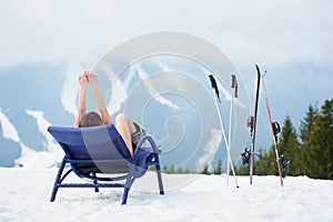 female skier on blue deck chair near skis at ski resort