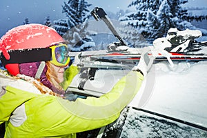 Female skier fastening skis to roof rails of car