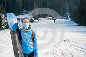 Female skier posing with a pait of skis wearing protective face mask.