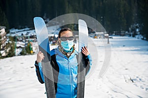 Female skier posing with a pait of skis wearing protective face mask.