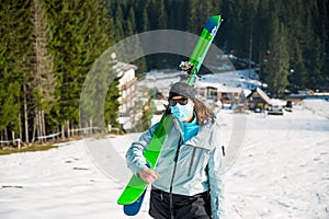 Female skier posing with a pait of skis wearing protective face mask.