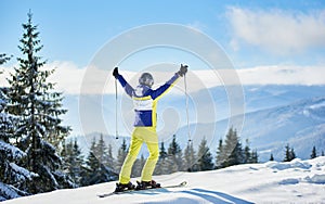 Female skier on snowy mountain top, rejoicing with hands up. Goal achievement concept. Picturesque landscape. Back view.