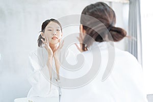 Female Skin Care. Young asian woman touching her face and looking to mirror in bathroom.