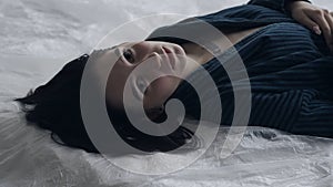 Female in sleepwear laying on the bed in the studio. Young woman in pajama shirt laying posing under thin sheet of