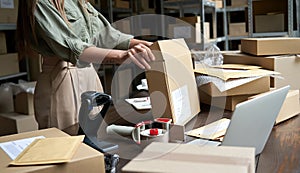 Female small business owner packing ecommerce order package in box at table.