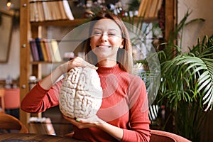 Female smiling psychologist holding human brain model at cabinet.