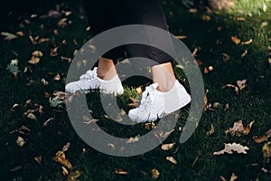 Female sneakers. White female shoes on feet. Sneakers closeup. Model posing in street, wearingwhite sneakers . Female fashion