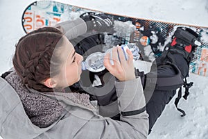 Female snowboarder is drinking for quenching the thirst