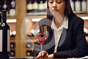 Female sommelier swirling red wine in glass on cellar background being in cellar. Wine expert exam to study different