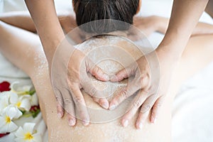 Female spa staff doing salt spa for Asian women. Young Asian woman having exfoliation treatment with body scrub in spa salon