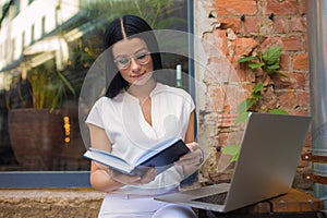 Female in spectacles smart student reading information from diary while preparing to exam college