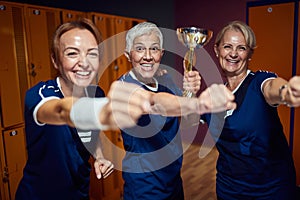 Female sports team of three celebrating together in locker room, holding golden cup