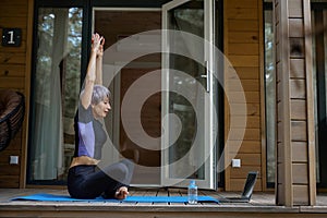 Female in sportswear does yoga in front of a laptop