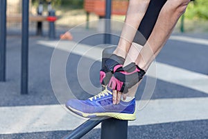 Female in sportswear and protective gloves ties bright sneakers preparing for a jog, run or other fitness. Morning workout on outd