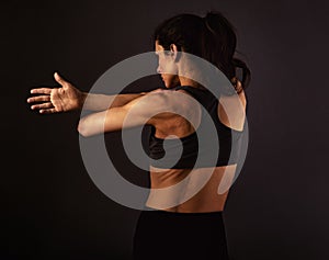 Female sporty muscular with ponytail doing stretching workout of the shoulders, blades in sport bra, holding the hands on the