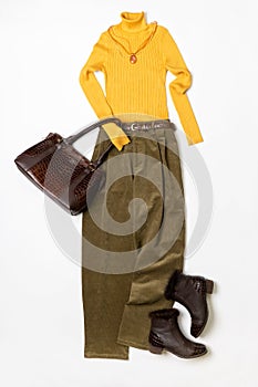 Female spring or autumn stylish clothing set. Yellow sweater and leather boots, green corduroy trousers, handbag. Trendy