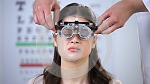 Female squeezing eyes, oculist putting refractor on smiling lady patient, lenses