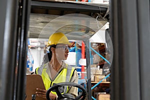 Female staff writing on clipboard while sitting on forklift