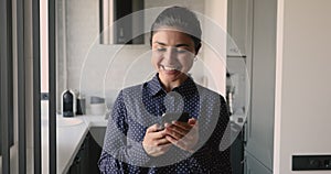 Female standing indoors holding smartphone got pleasant message feels happy