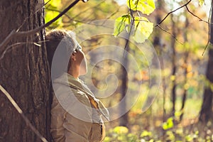 Female standing near big maple tree in park and listen sounds or music in the autumn forest. Concept. Indian summer season
