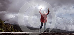 Female standing with success with fists raised up on peak of mountain with sky background.  Achievement and winning concept